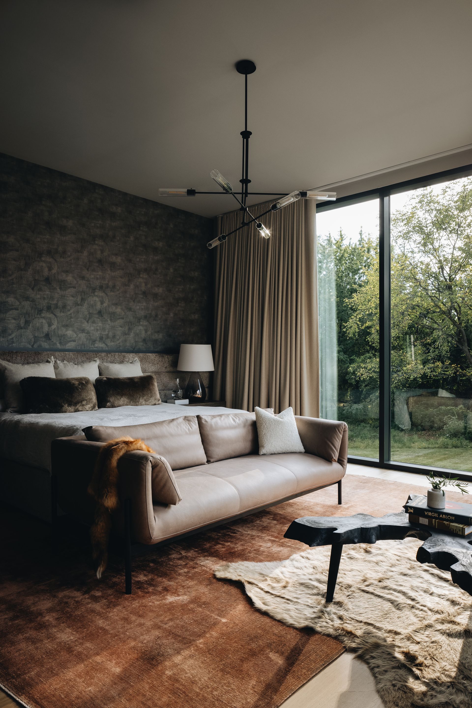 Modern living room with gray sofa, dark accent wall, and floor-to-ceiling windows overlooking greenery
