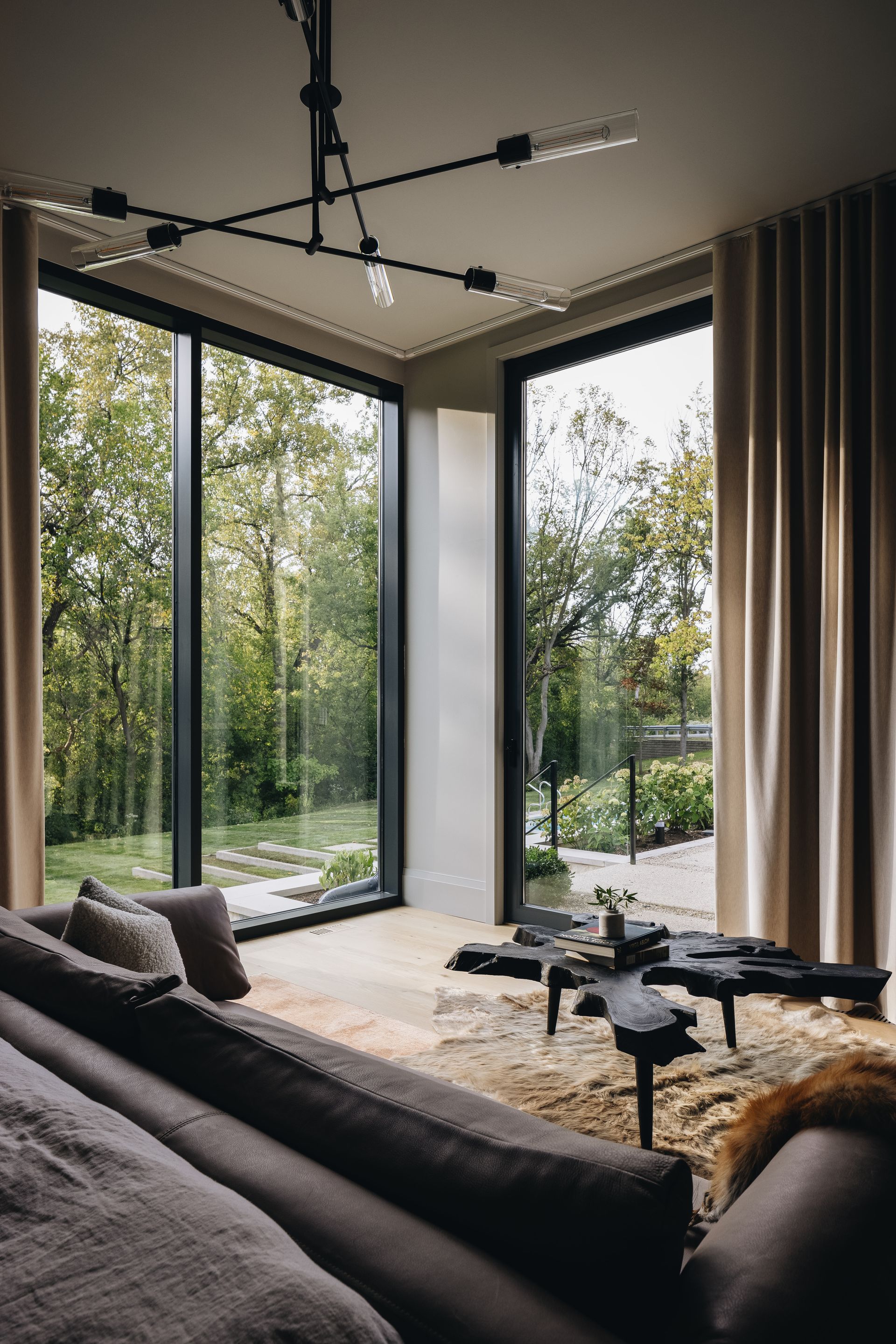 Modern living room with floor-to-ceiling windows, dark sofa, and a round coffee table overlooking trees.
