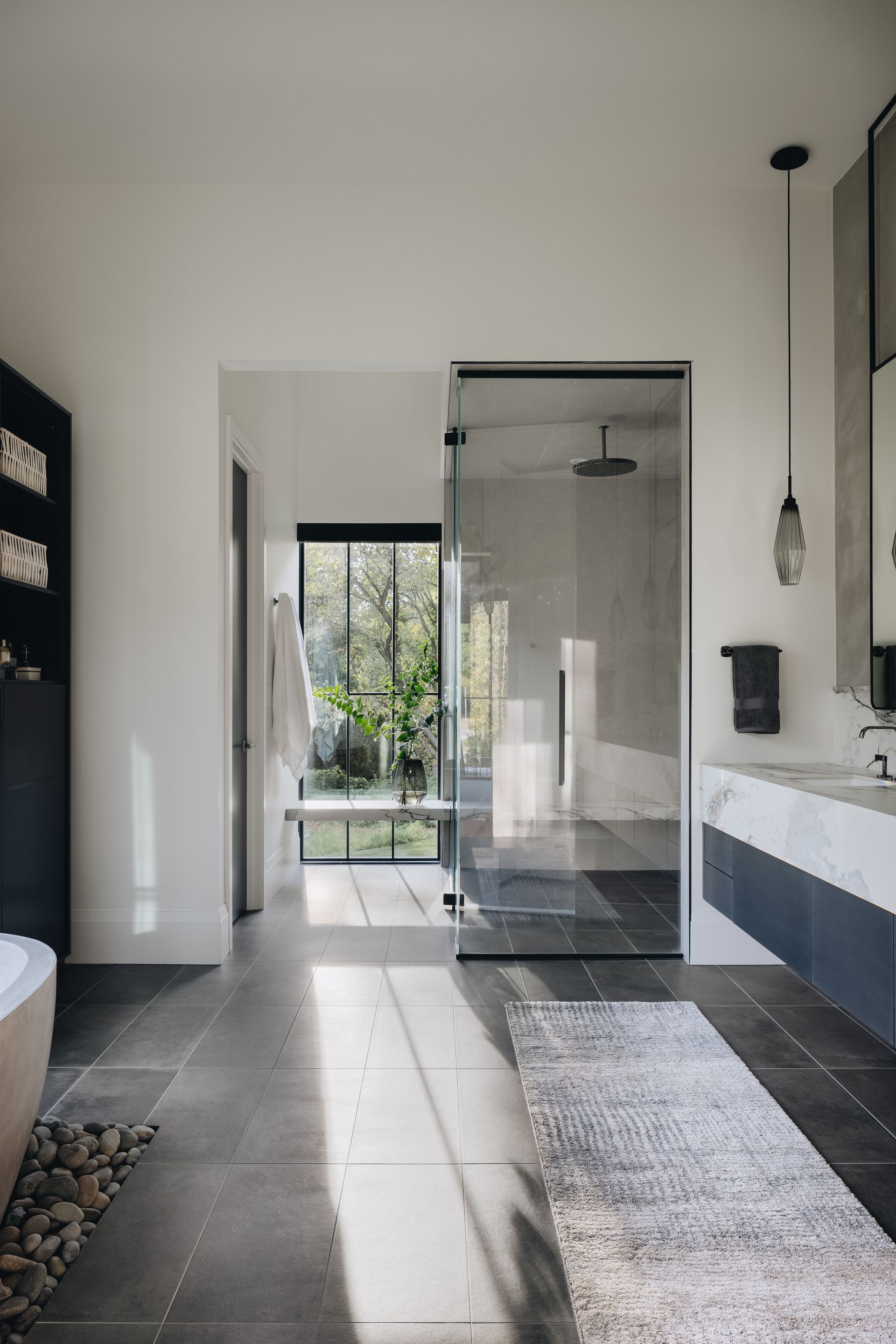 Modern bathroom with a glass shower, dark tile floor, floating sink, and large window to a garden.