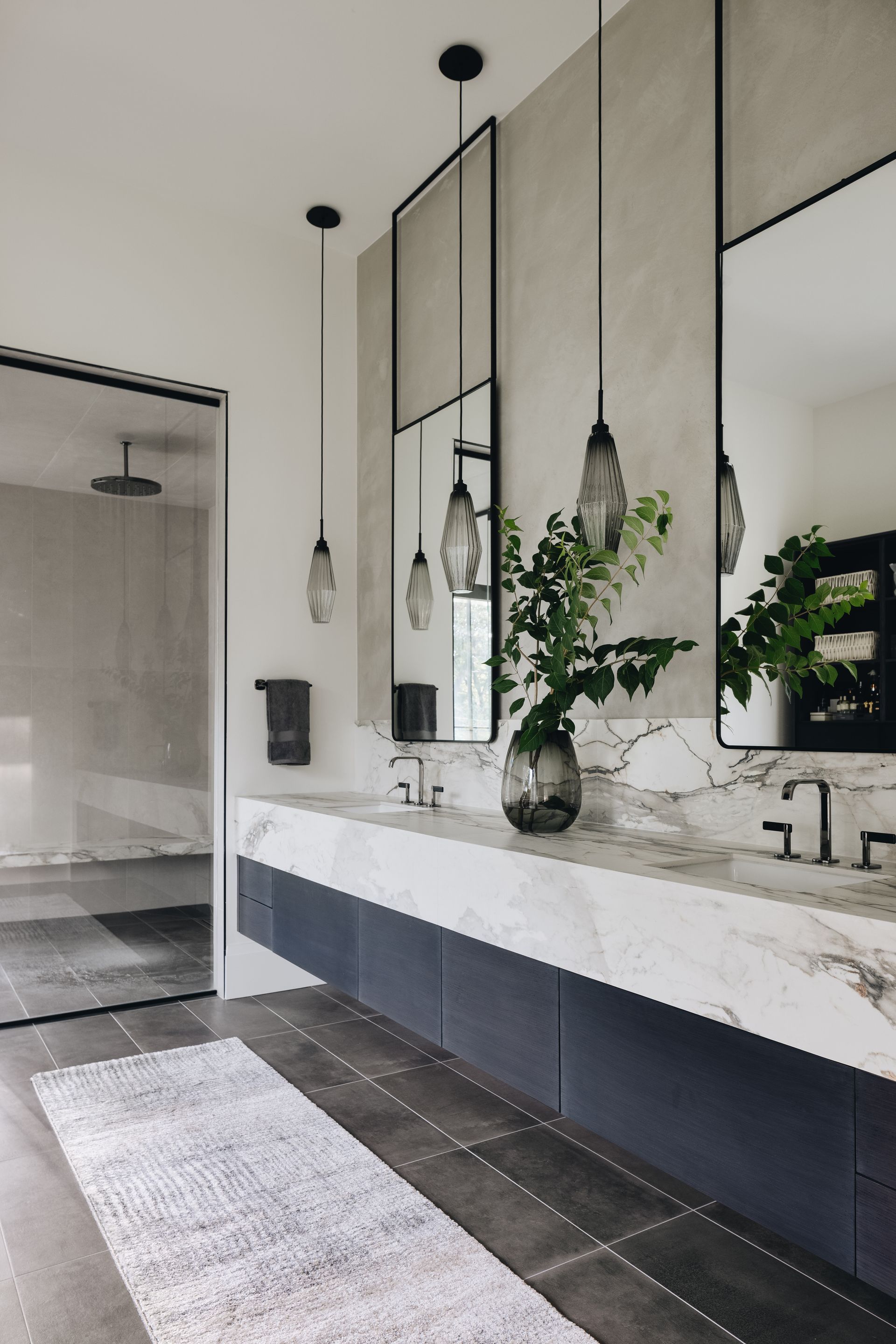 Modern bathroom vanity with large mirrors, hanging pendant lights, and a marble countertop with greenery