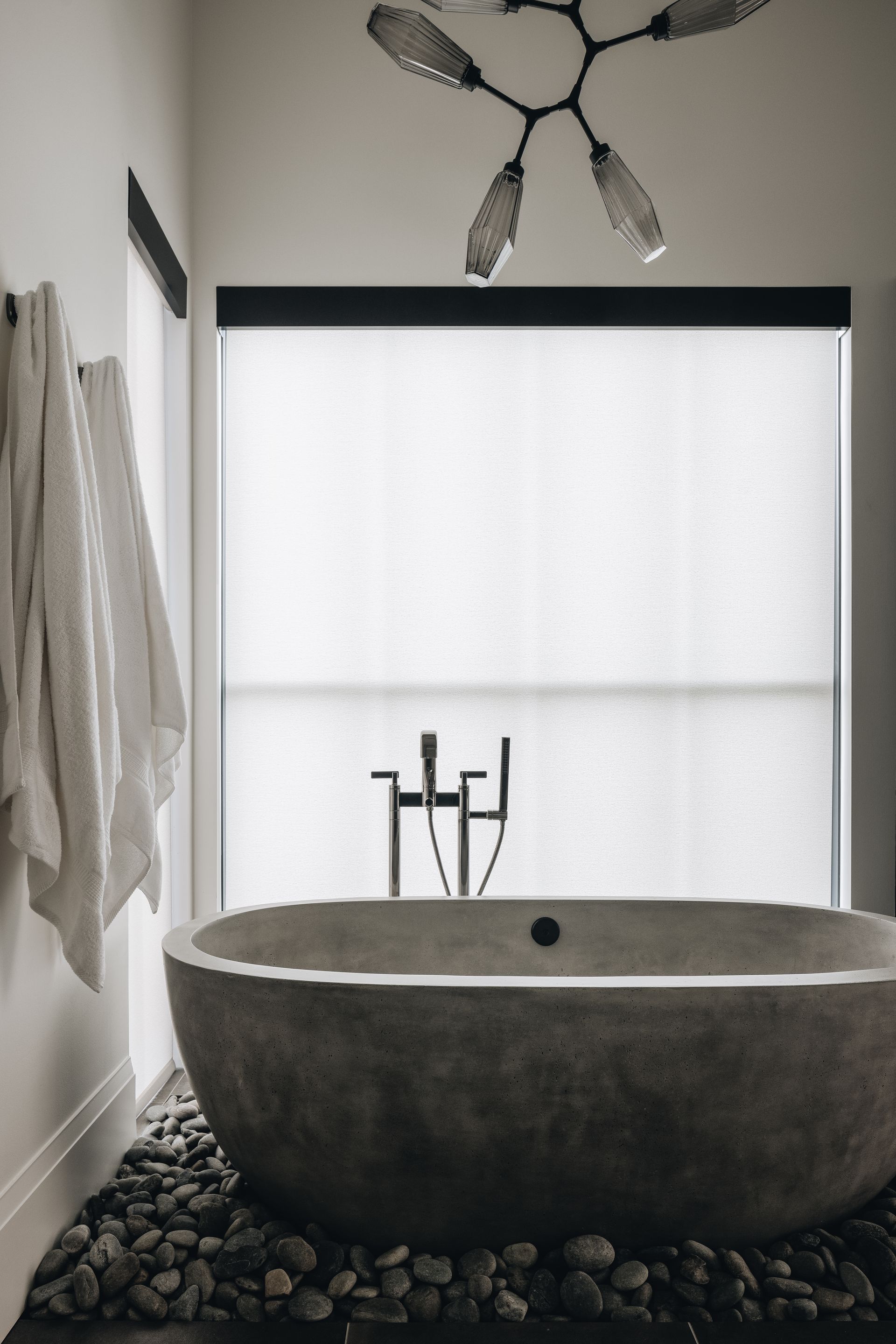 Modern bathroom with oval stone tub, pebble floor, and frosted window light