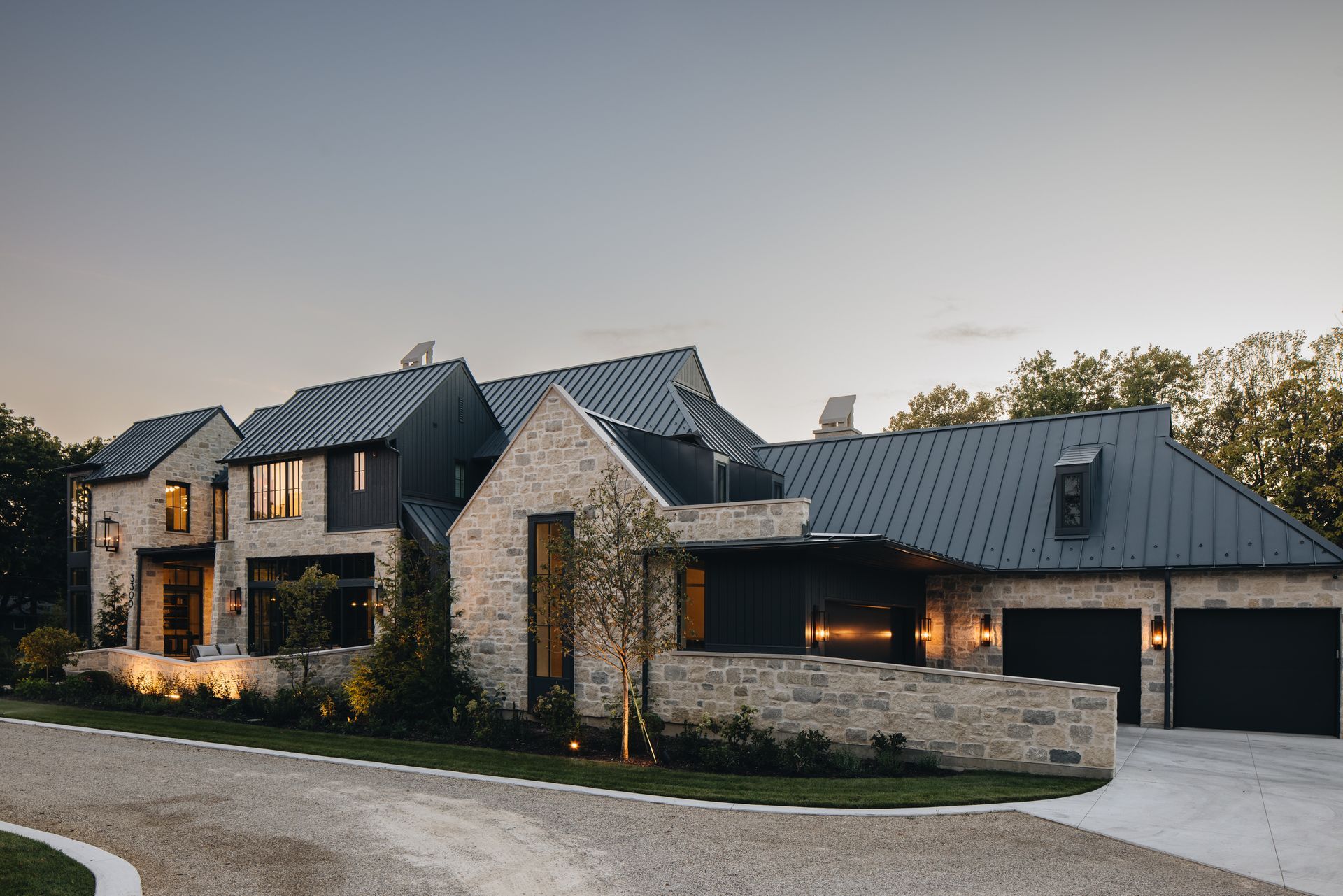 Modern stone house with dark metal roof and garage at dusk