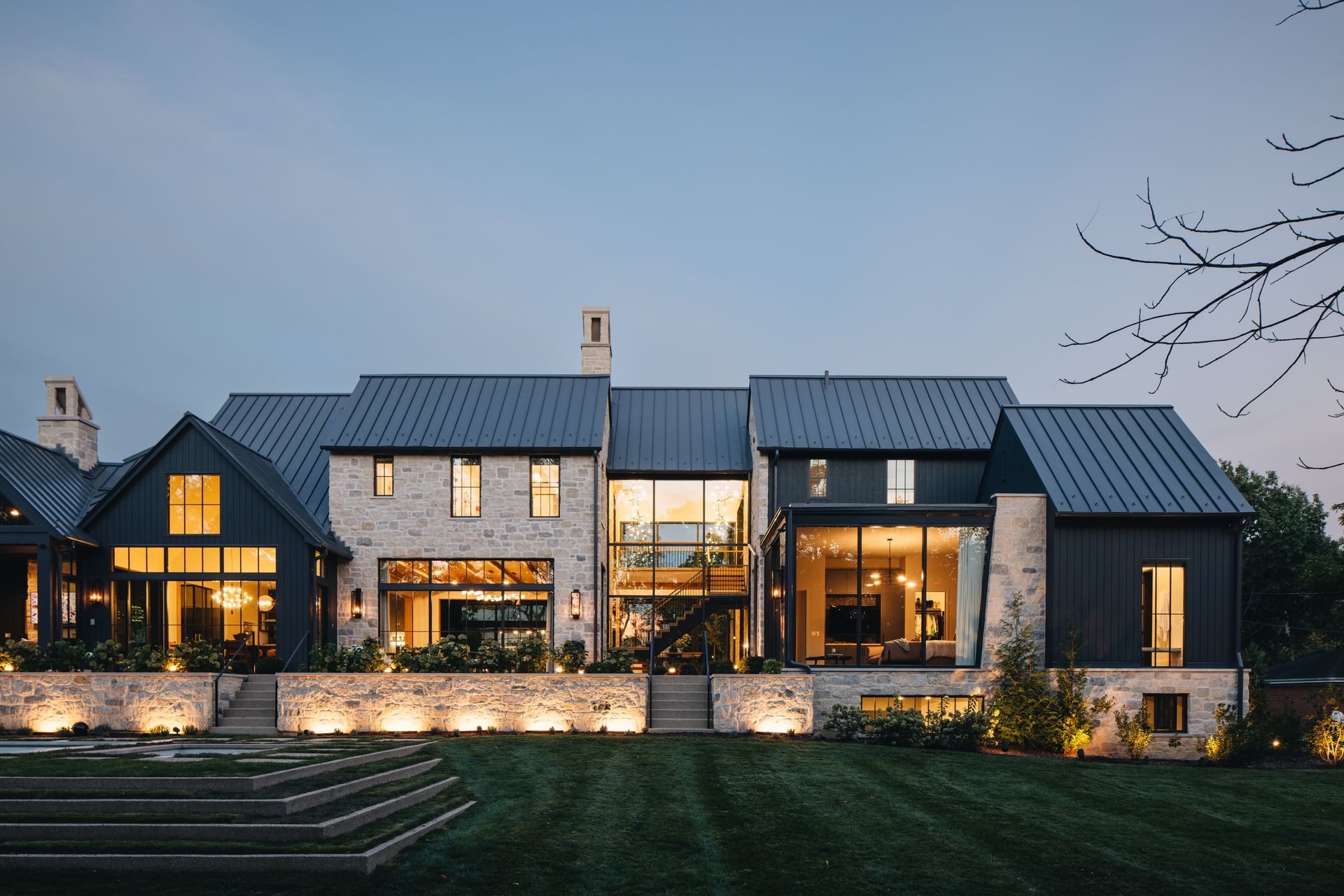 Modern stone house with lit windows and warm exterior lighting at dusk