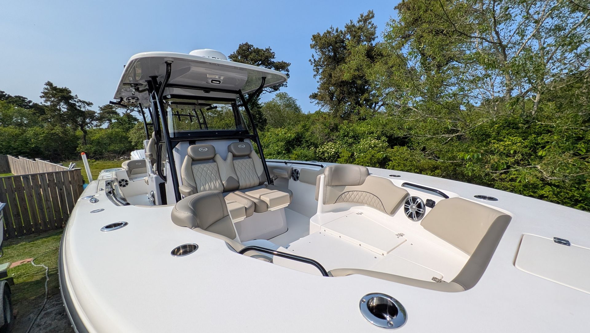 A white boat is parked in the grass in front of a fence.