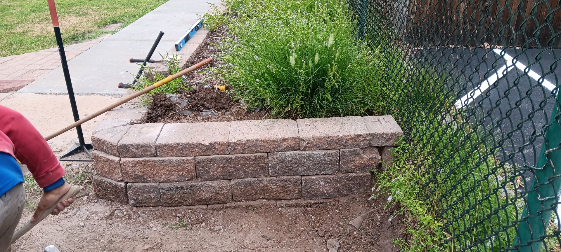 A person is working on a brick wall next to a chain link fence.