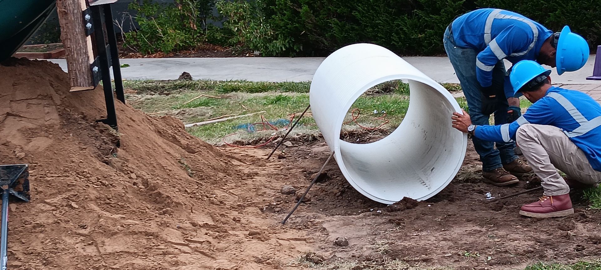 Two construction workers are working on a large white pipe in the dirt.