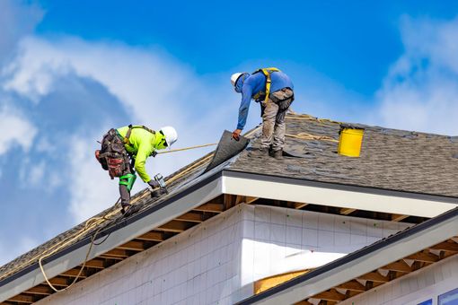 Roofers working on a house roof, repairing shingles under a blue sky Roofers working on a house roof, repairing shingles under a blue sky