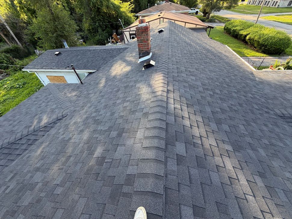Aerial view of a gray shingled roof with chimneys and surrounding trees and houses