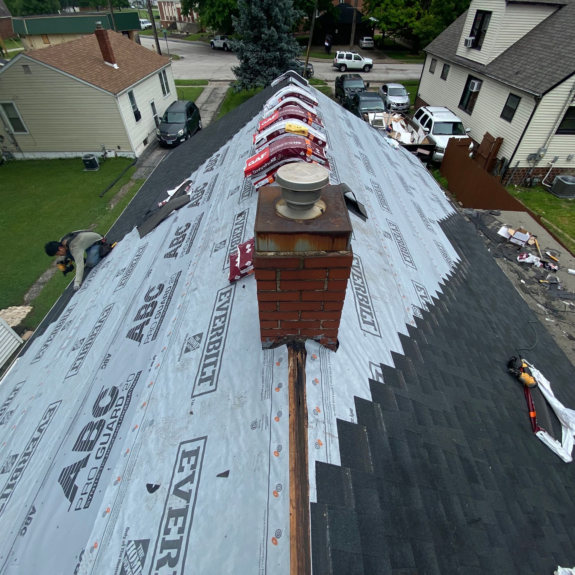 Roofer working on a brown shingled roof with vents and utility lines nearby Roofer working on a brown shingled roof with vents and utility lines nearby