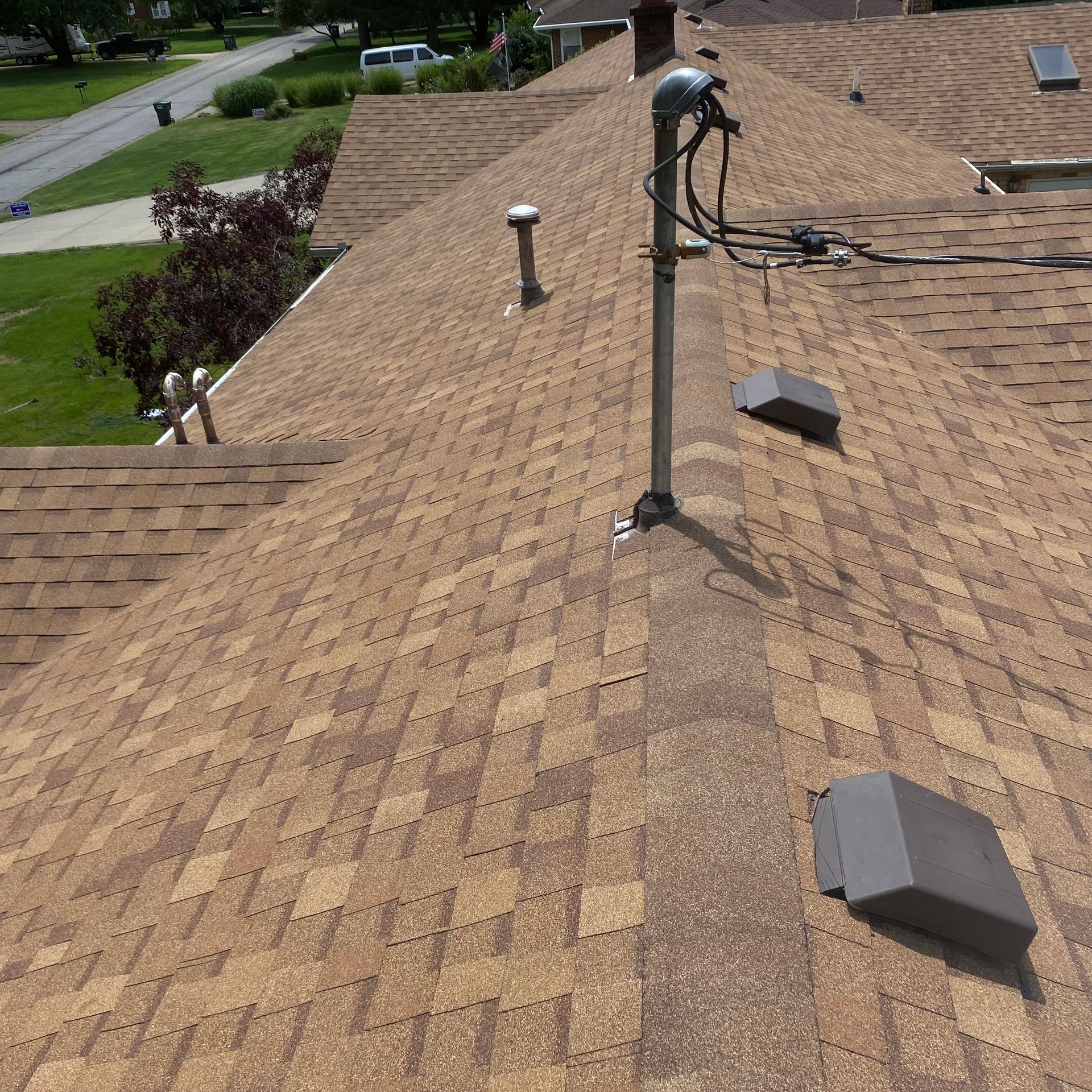Roofer working on a tan shingle roof with vents and cables on a sunny day