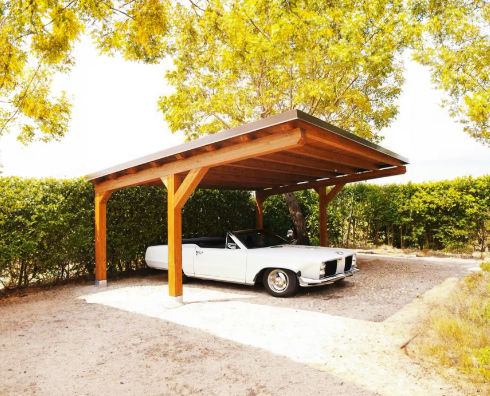 A white car is parked under a wooden carport