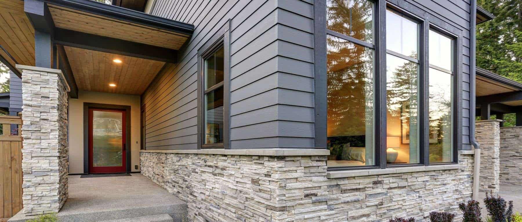 The front of a house with a stone wall and a blue siding.