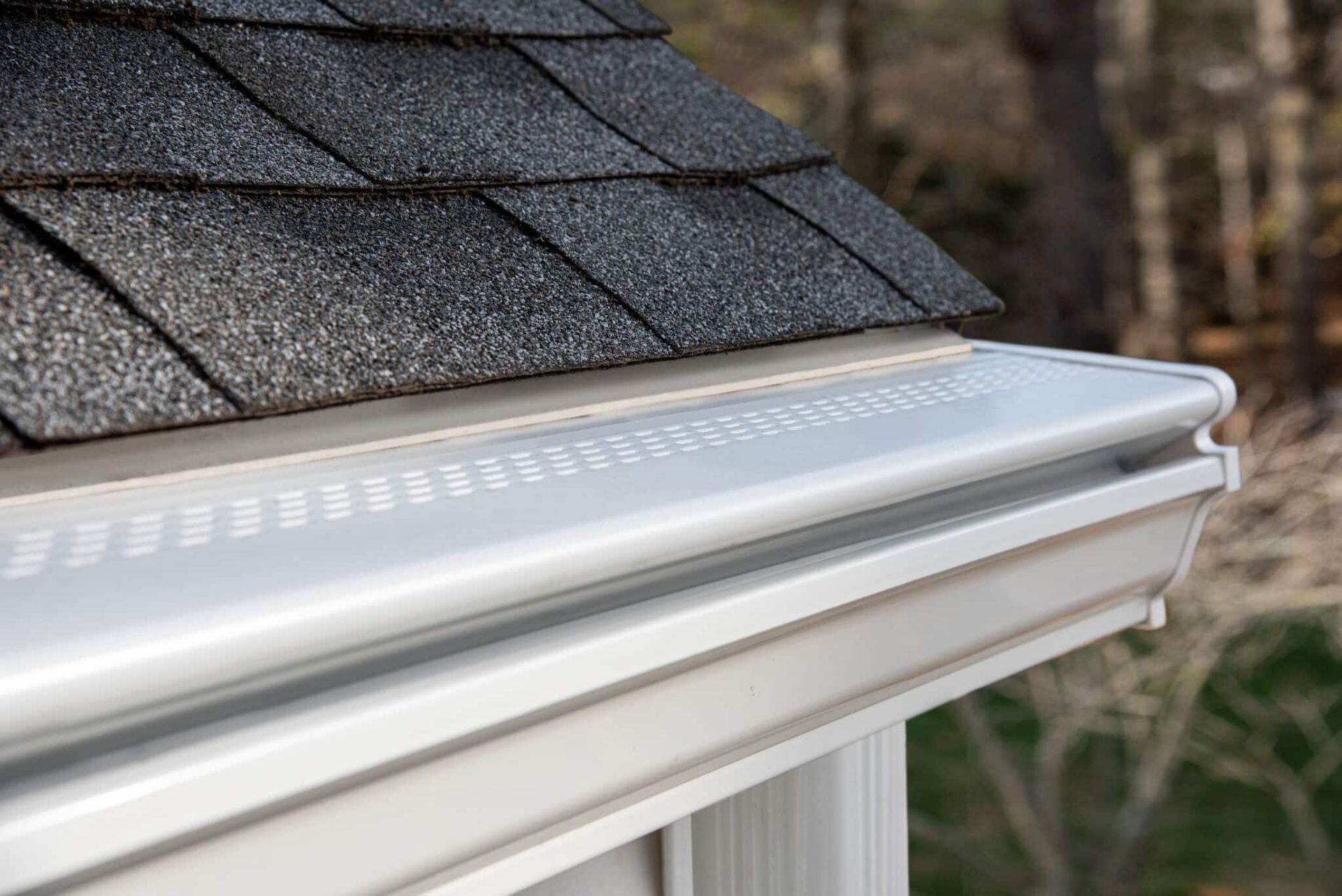 A close up of a gutter on the side of a house with a roof in the background.