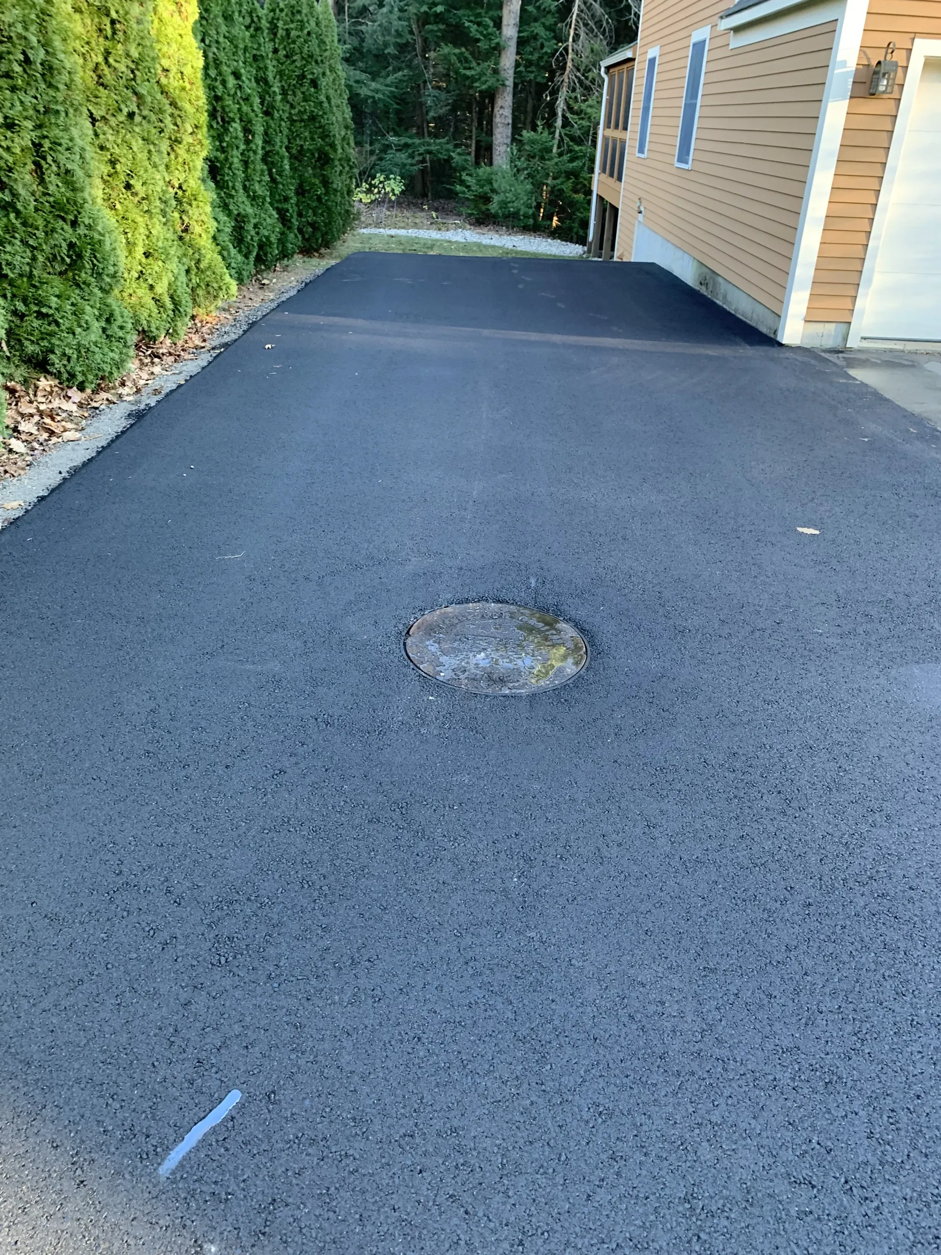 Newly paved asphalt driveway with a circular utility cover in the center.