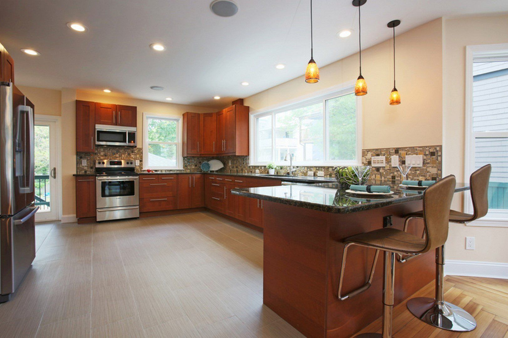 A modern kitchen featuring wood cabinets, stainless steel appliances, a granite-topped island, and two bar stools.