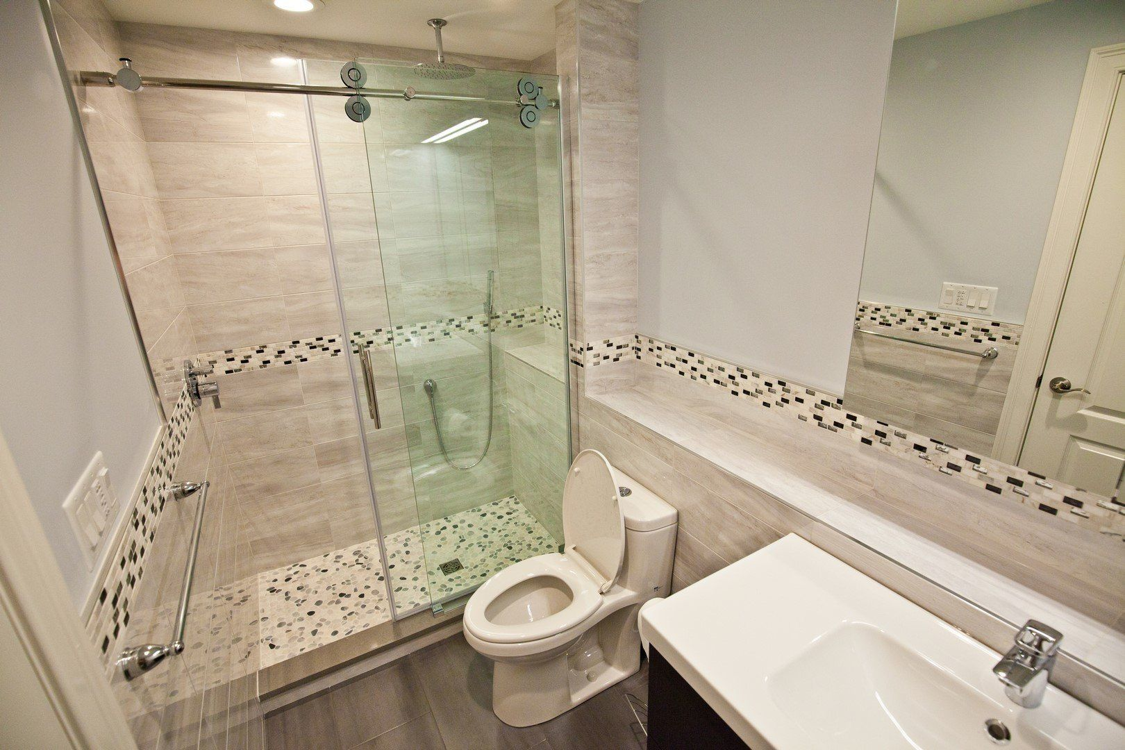 A modern bathroom featuring a glass-enclosed shower with pebble-tile flooring, a white toilet, and a vanity with a sink.