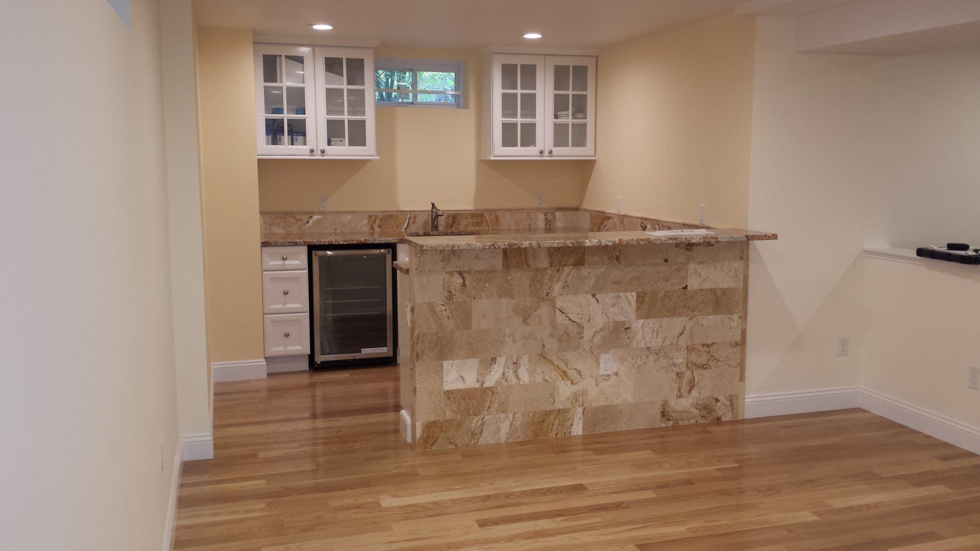 A finished basement wet bar featuring stone fronting, granite countertops, white cabinetry, and a beverage refrigerator.
