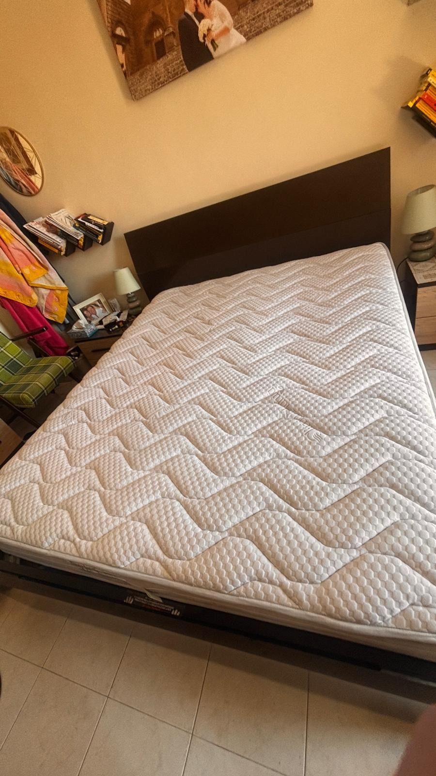 Camera da letto con letto in legno scuro e materasso bianco a fantasia su pavimento piastrellato.