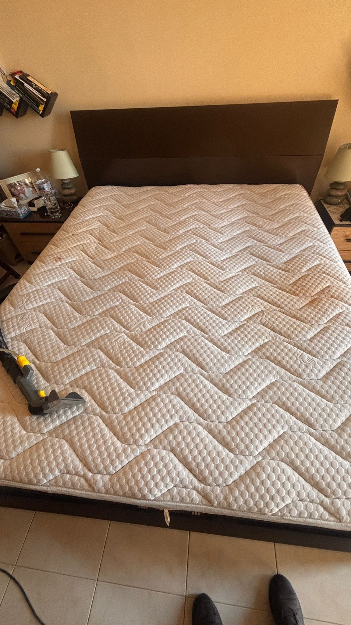 Letto con trapunta a spina di pesce beige e testiera scura in una camera da letto, visto dalla pediera.