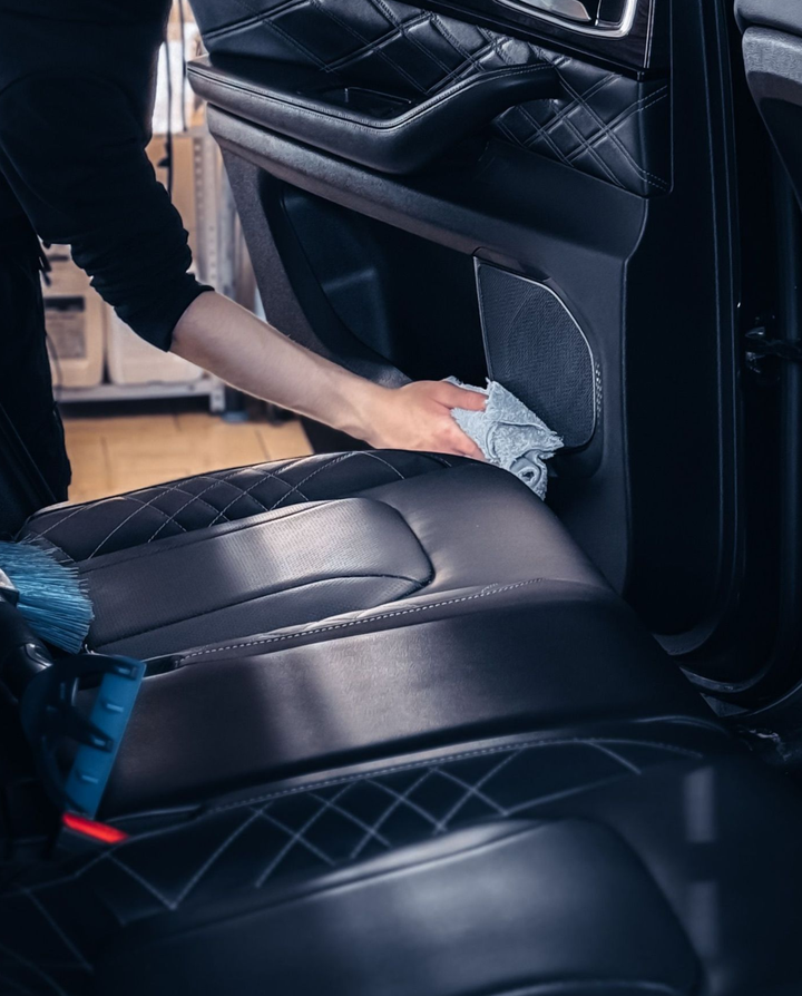Una persona pulisce con un panno un sedile di pelle nera all'interno di un'auto.