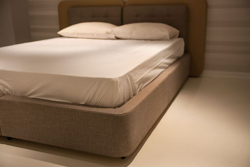 Letto moderno con biancheria da letto beige in una camera da letto illuminata da una luce soffusa.
