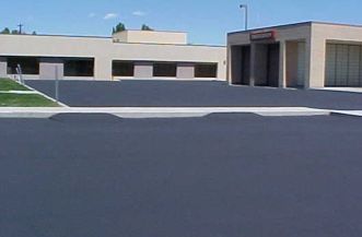 Low school building with a large empty asphalt lot in front