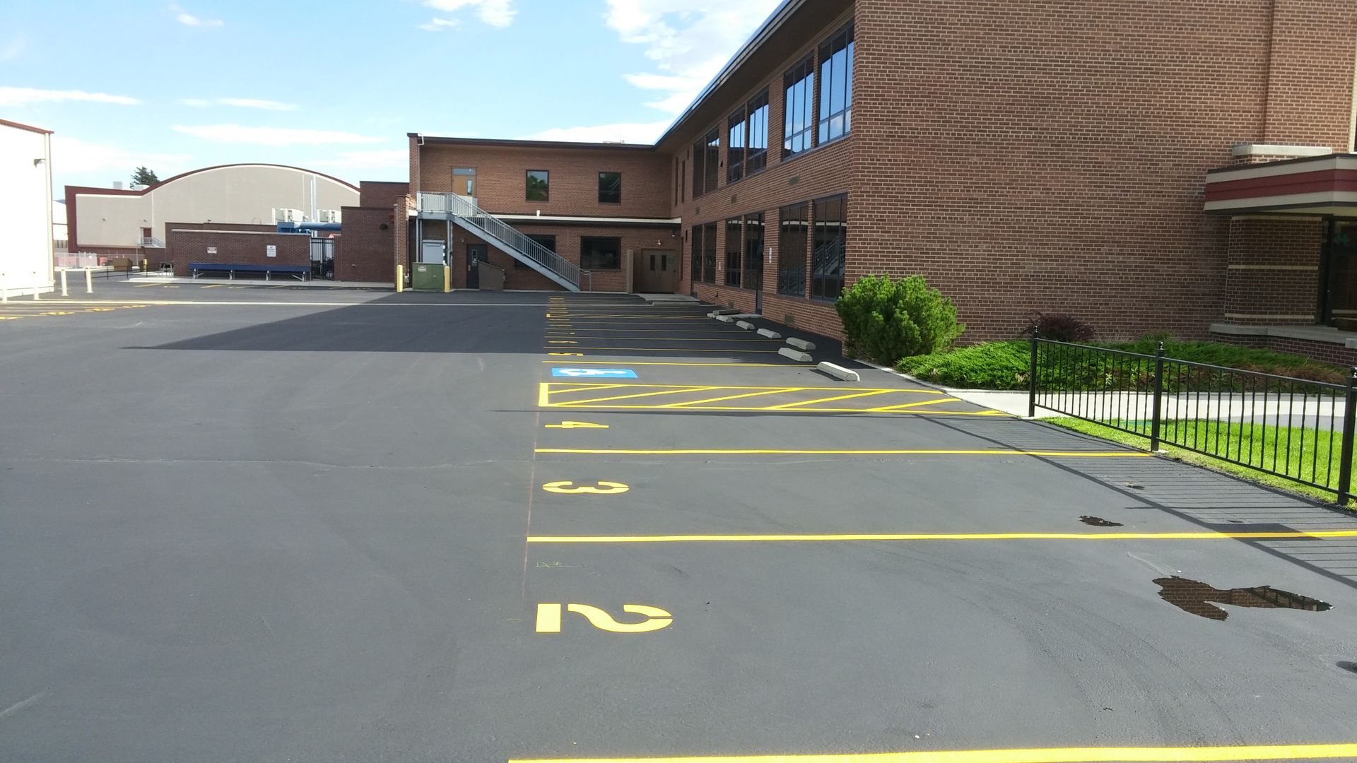 Empty school parking lot beside a brick building, with yellow numbered spaces painted on the asphalt.