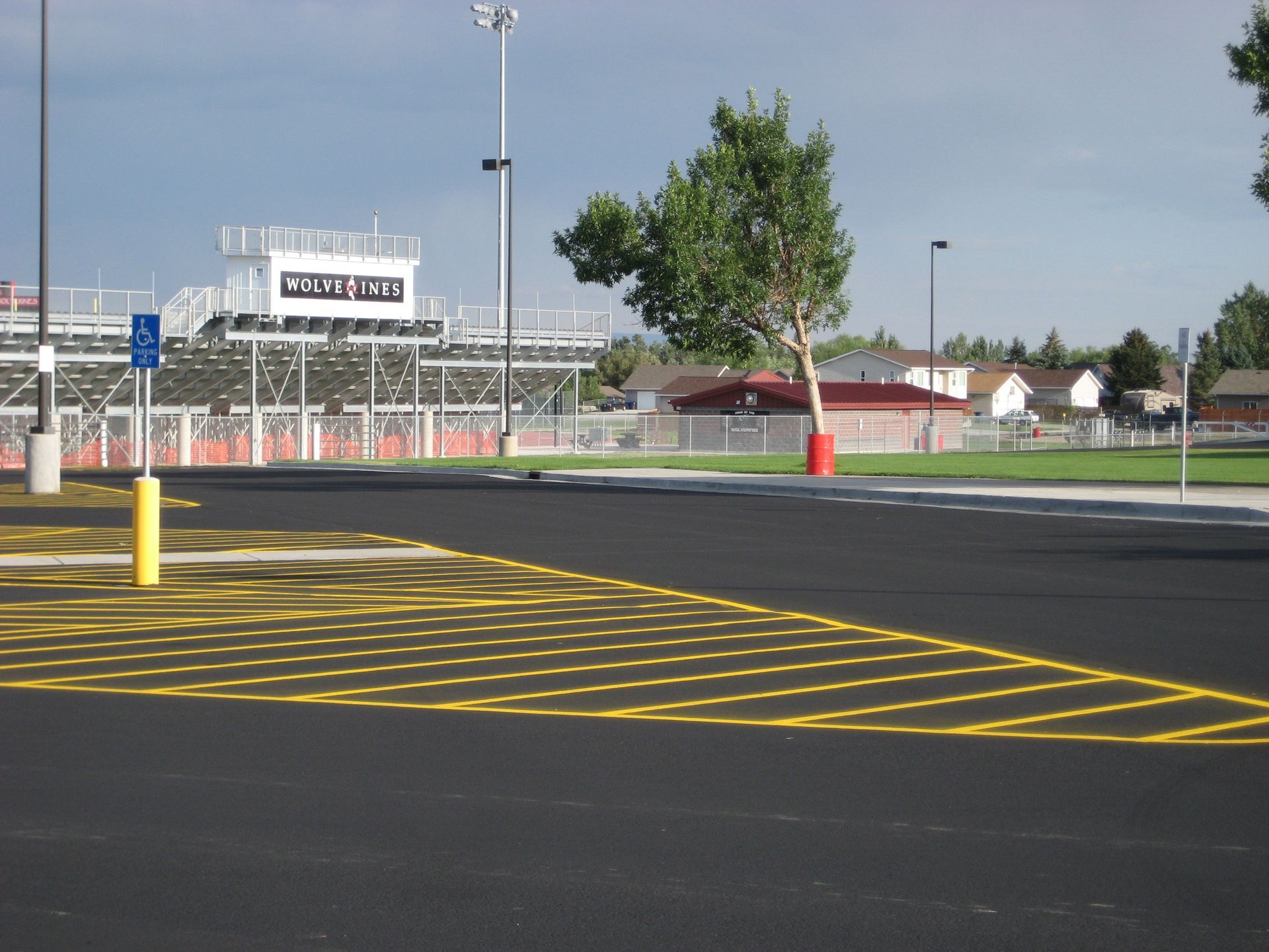 Empty parking lot with yellow diagonal markings, a few poles, and a sports stadium in the background