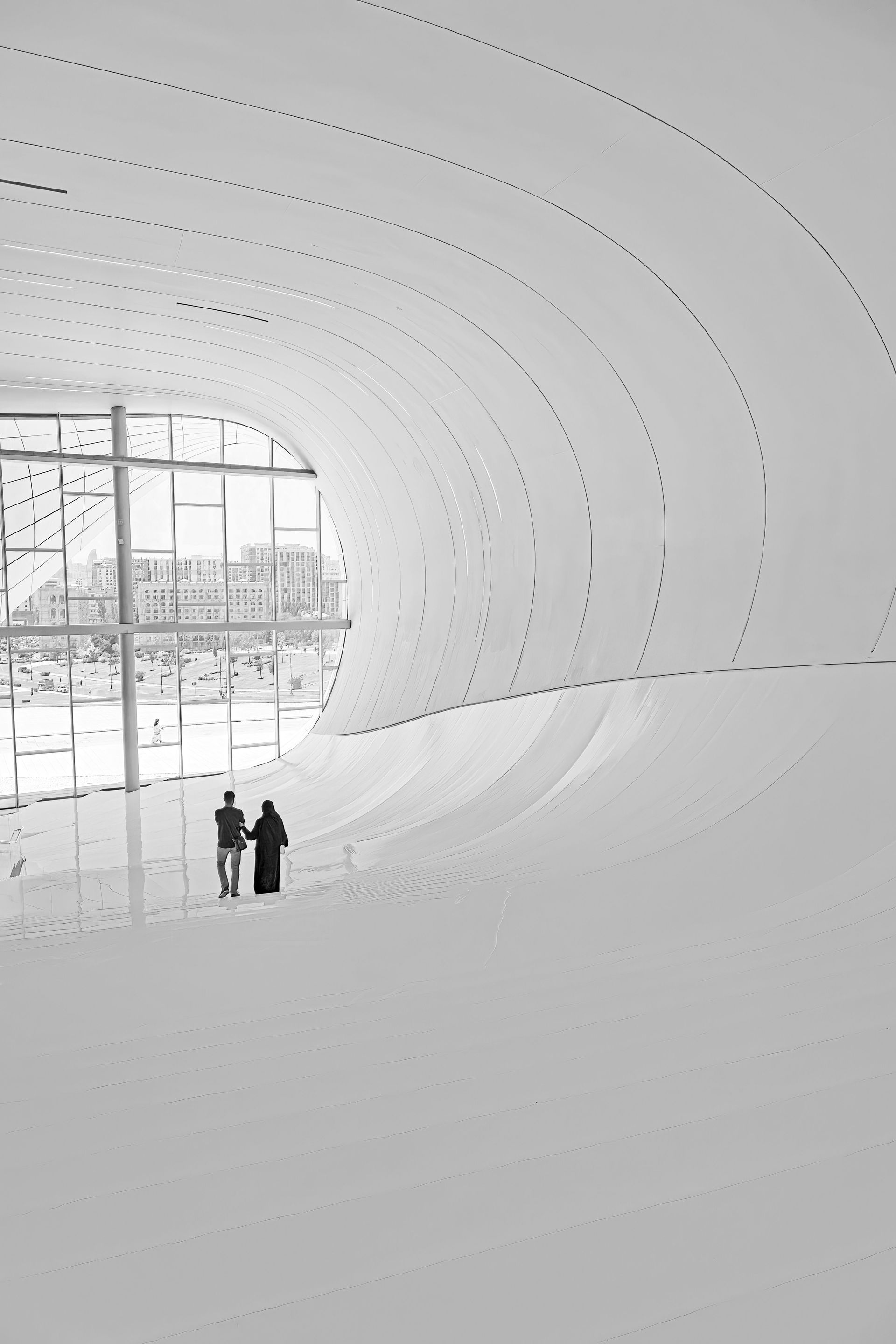 Minimal white interior with two people standing near a large curved wall and window.