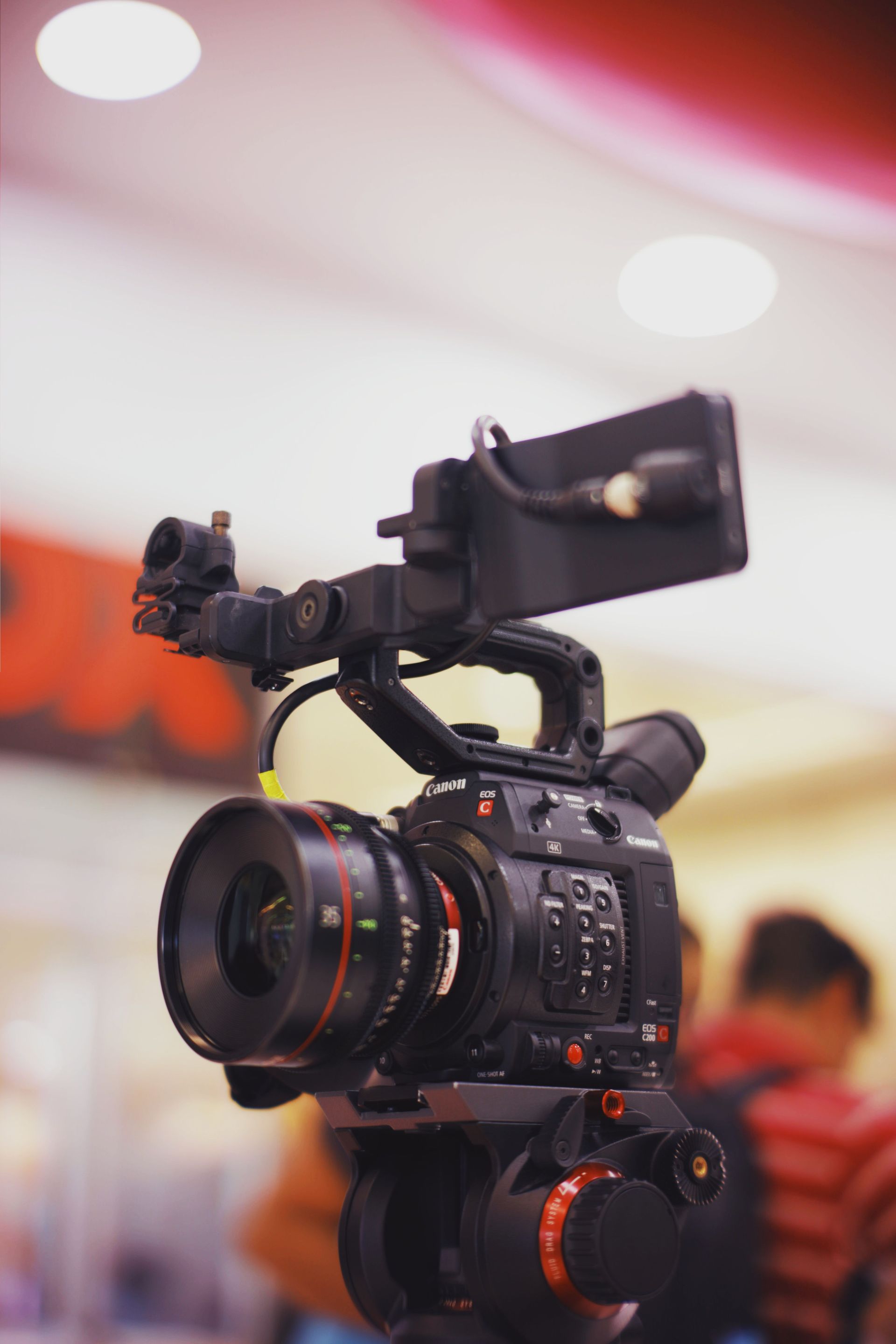 Professional video camera on a tripod with a monitor, indoors with blurred people and lights in the background