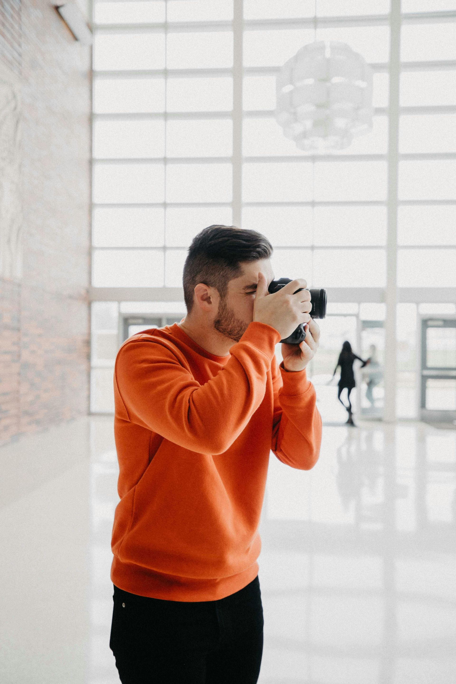 Man in an orange sweater photographing in a bright, modern lobby