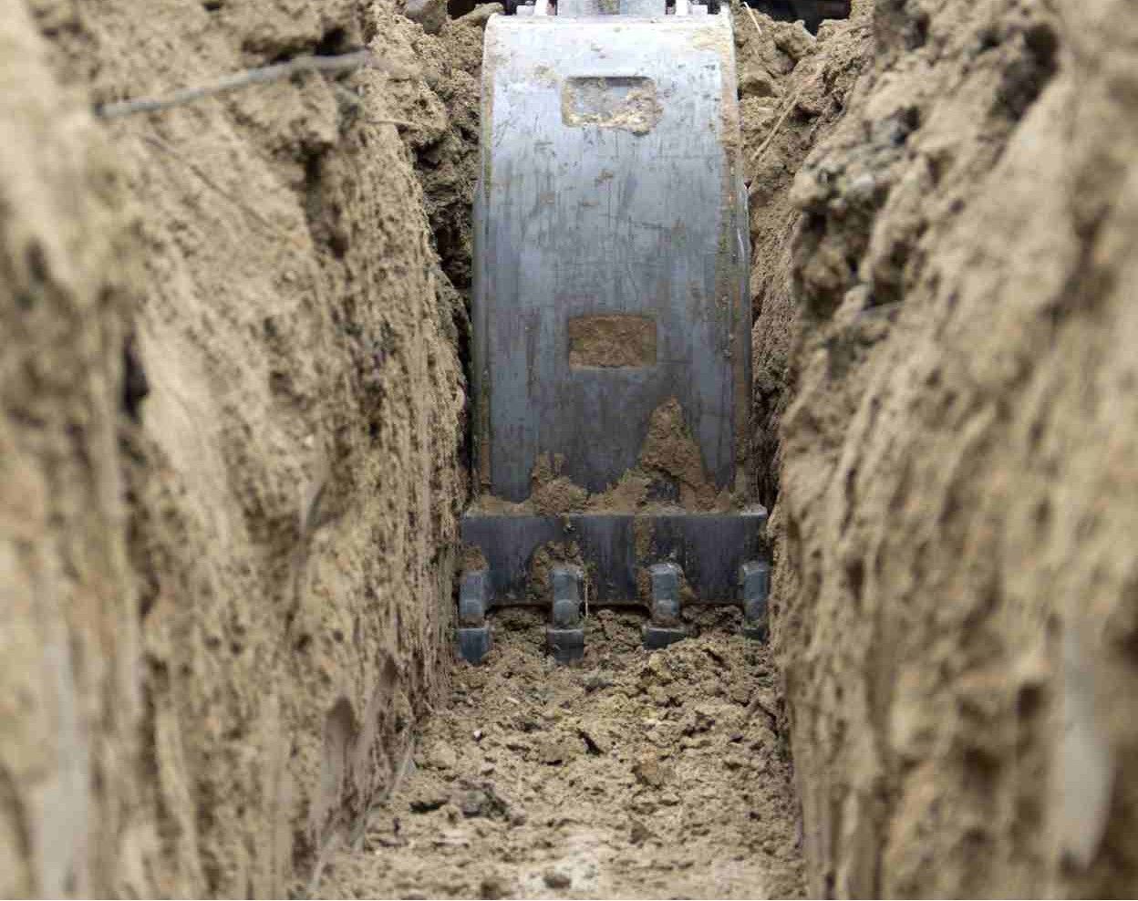 Excavator bucket digging a narrow trench