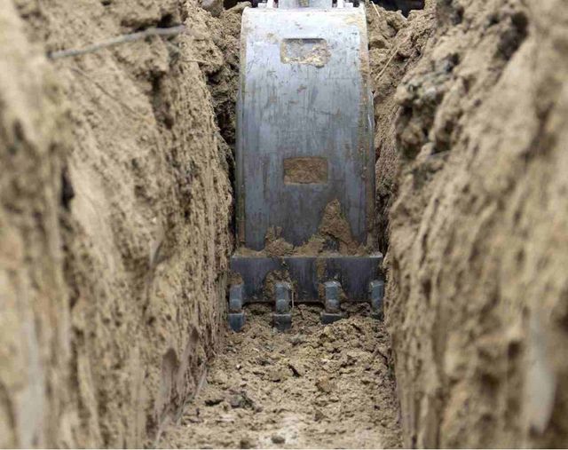 Excavator bucket digging a narrow trench