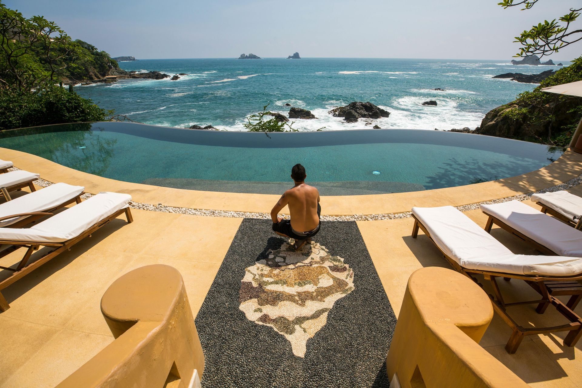 Man meditating by infinity pool overlooking the ocean.