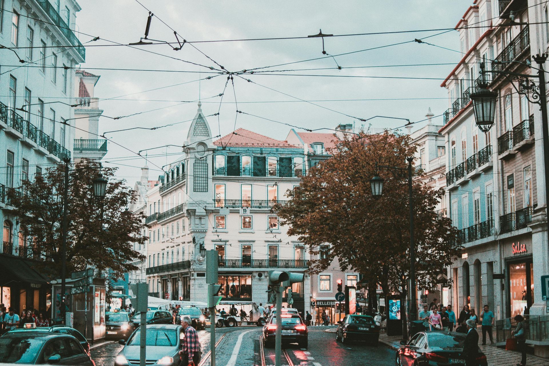 City street scene with buildings, traffic, and overhead wires under a cloudy sky.