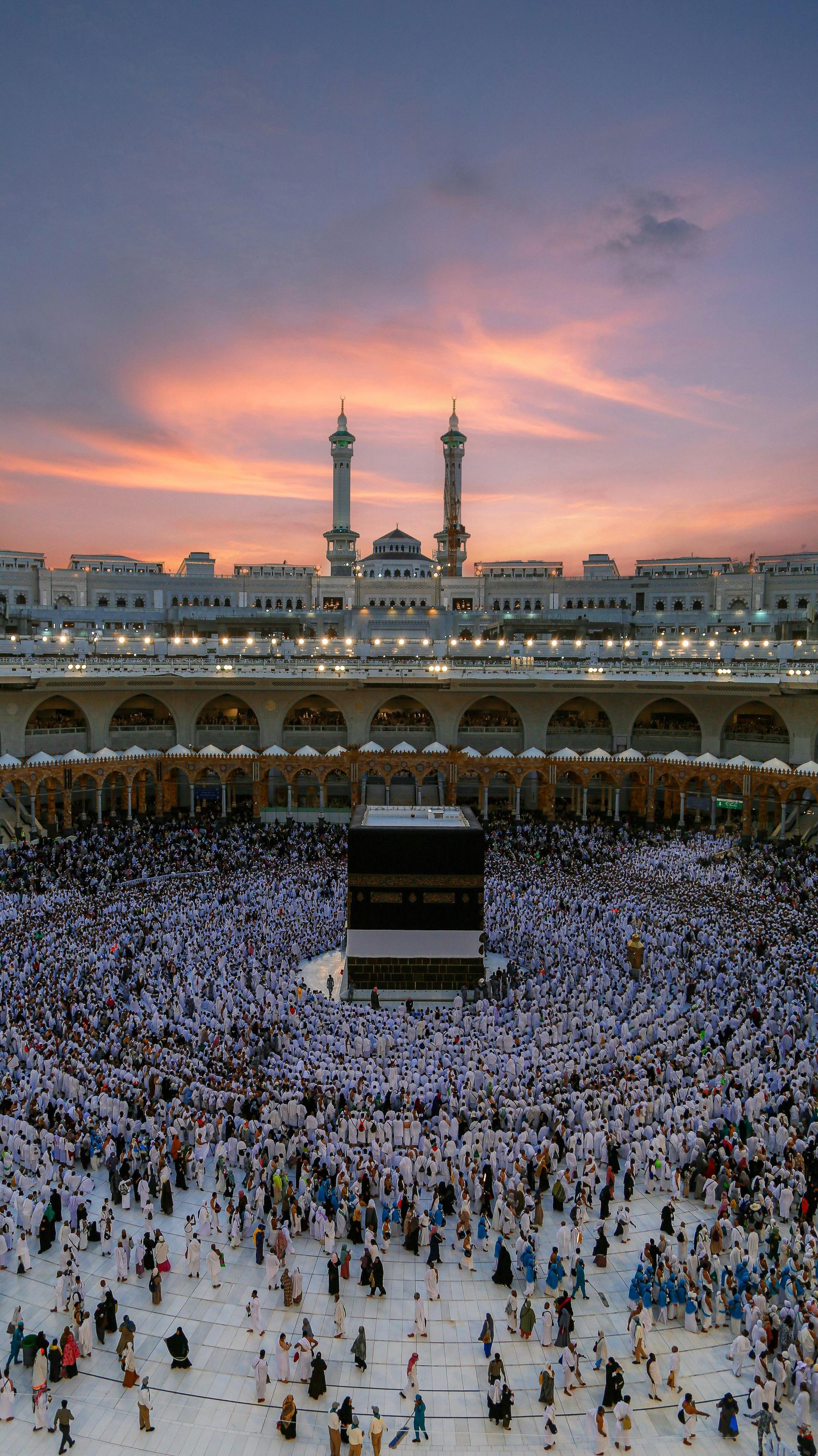 The Kaaba in Mecca, surrounded by many people in white robes; sunset sky.