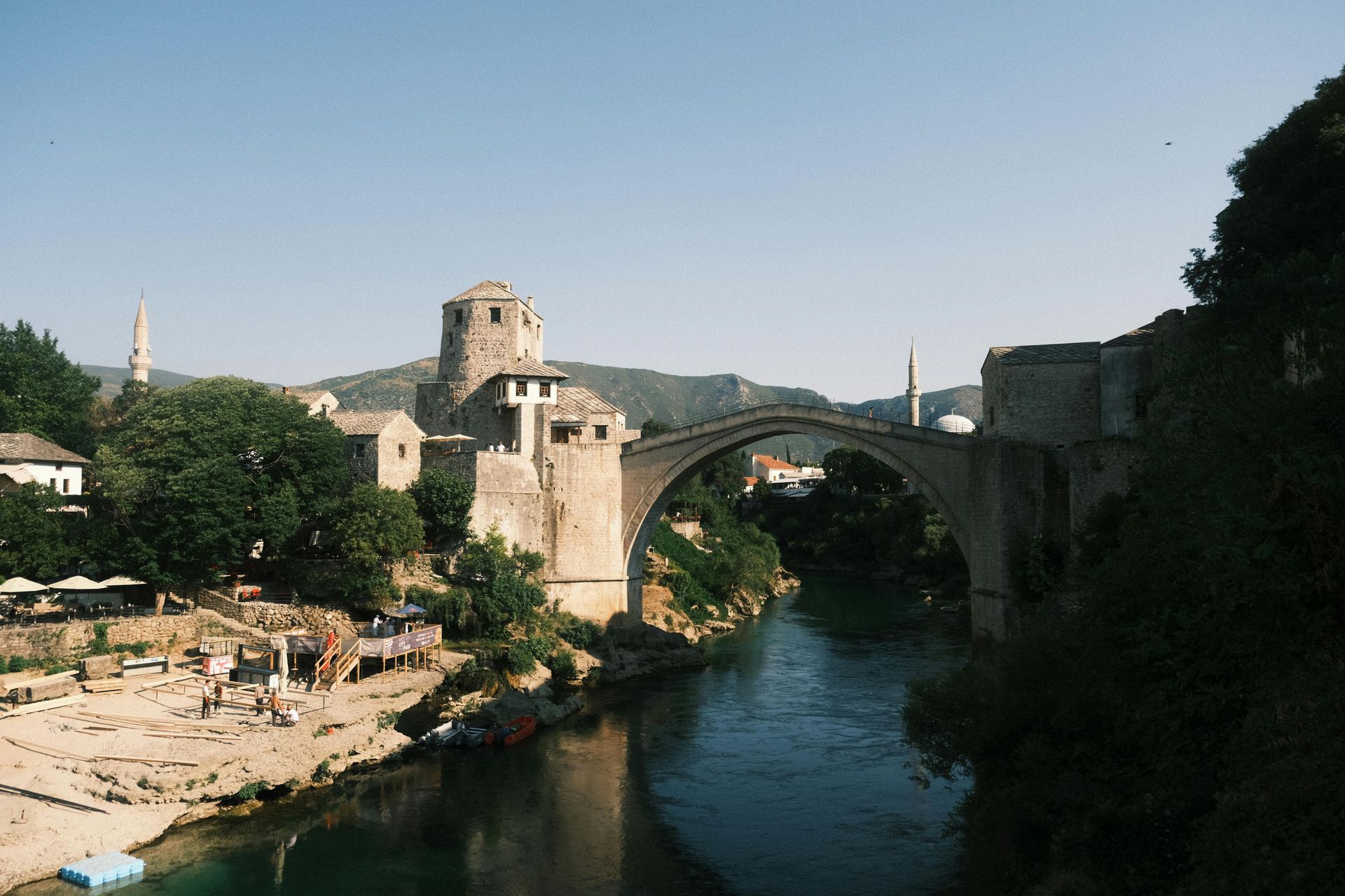 Stone bridge over a river in Mostar, Bosnia. Buildings and trees flank the water.