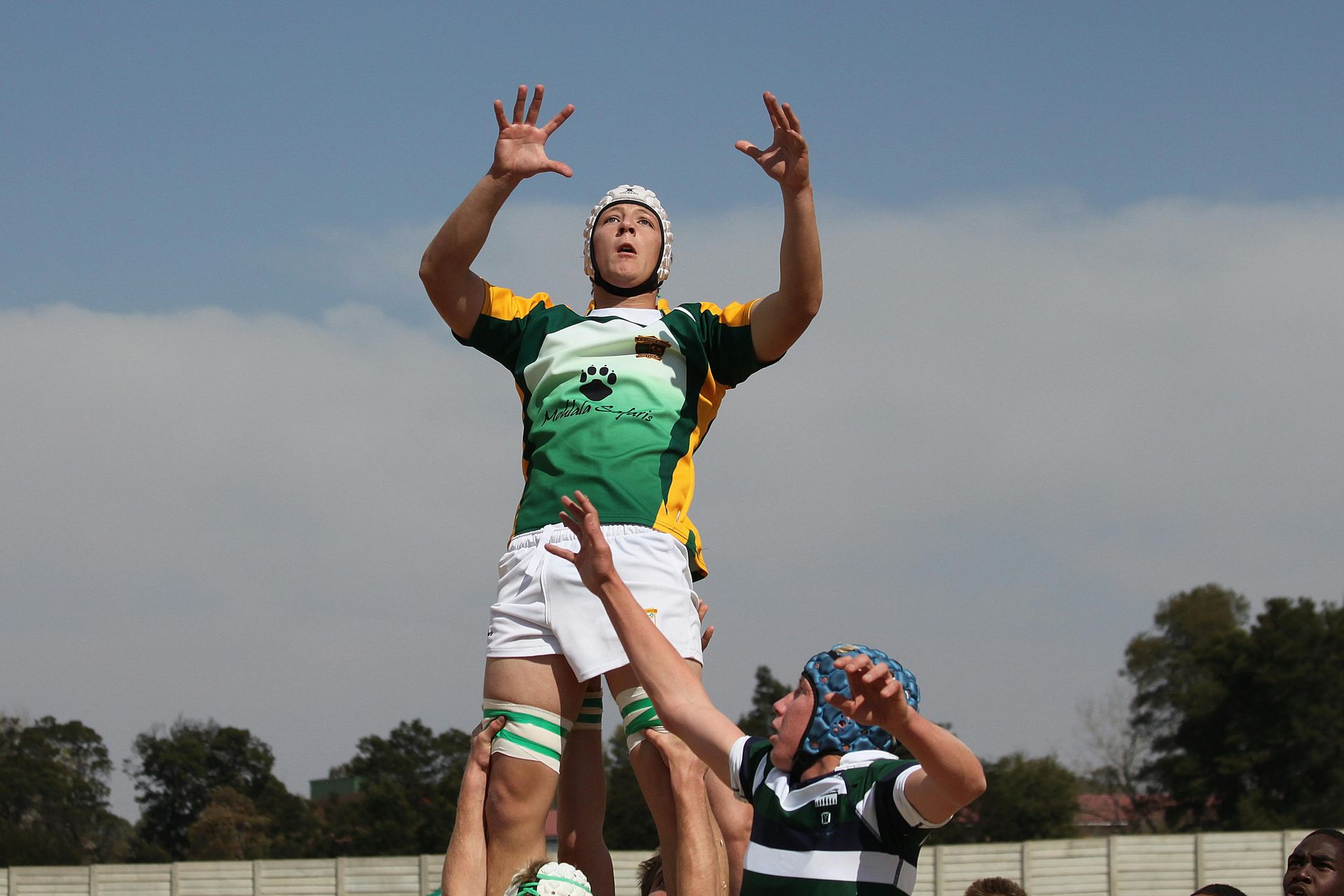 Rugby player in green and yellow jersey, jumping to catch ball, supported by teammates.