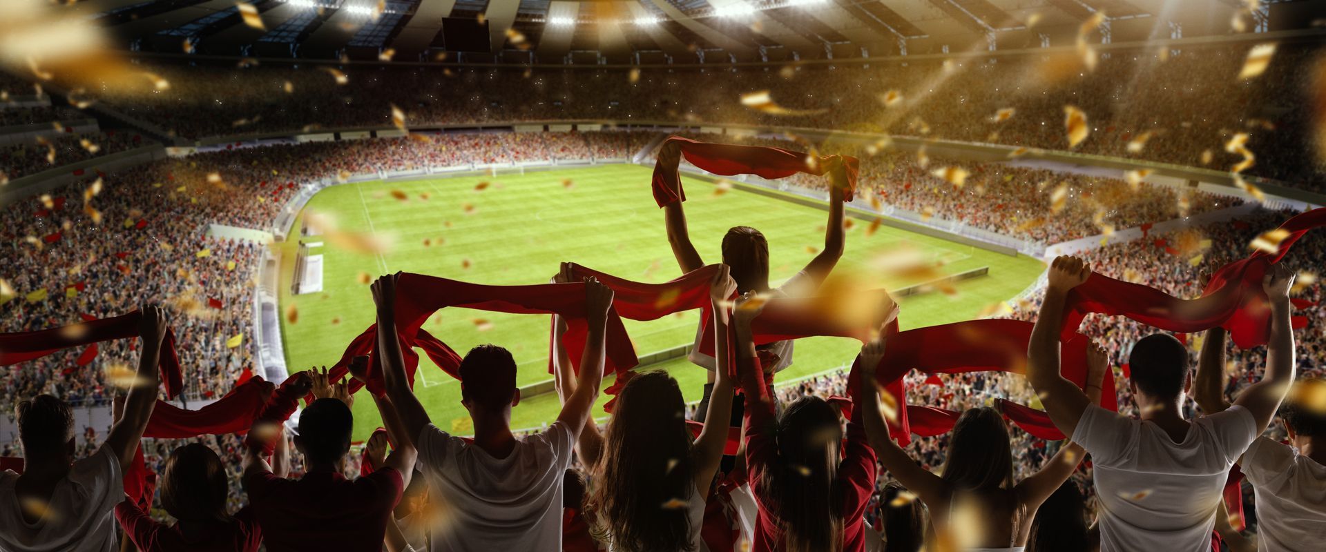 Fans celebrating with red scarves in a packed stadium with confetti falling, likely after a sports victory.