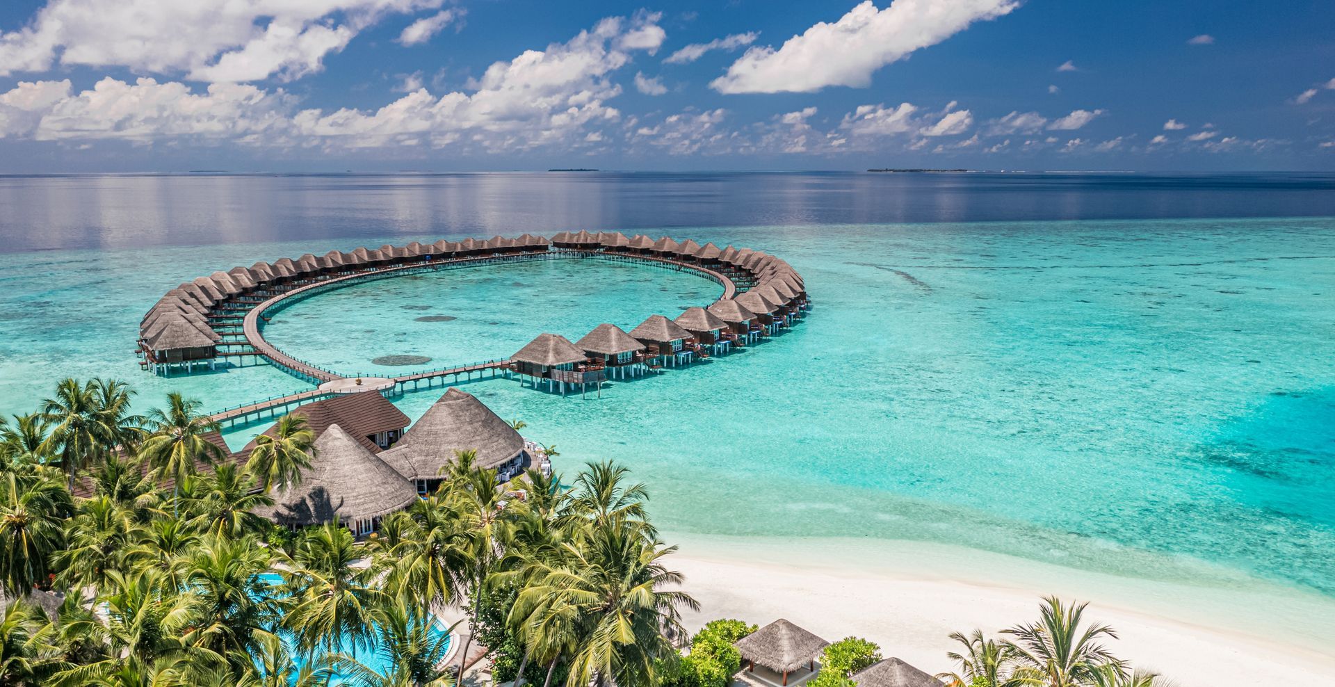 Overwater bungalows in turquoise water surrounding a tropical island, under a bright blue sky.