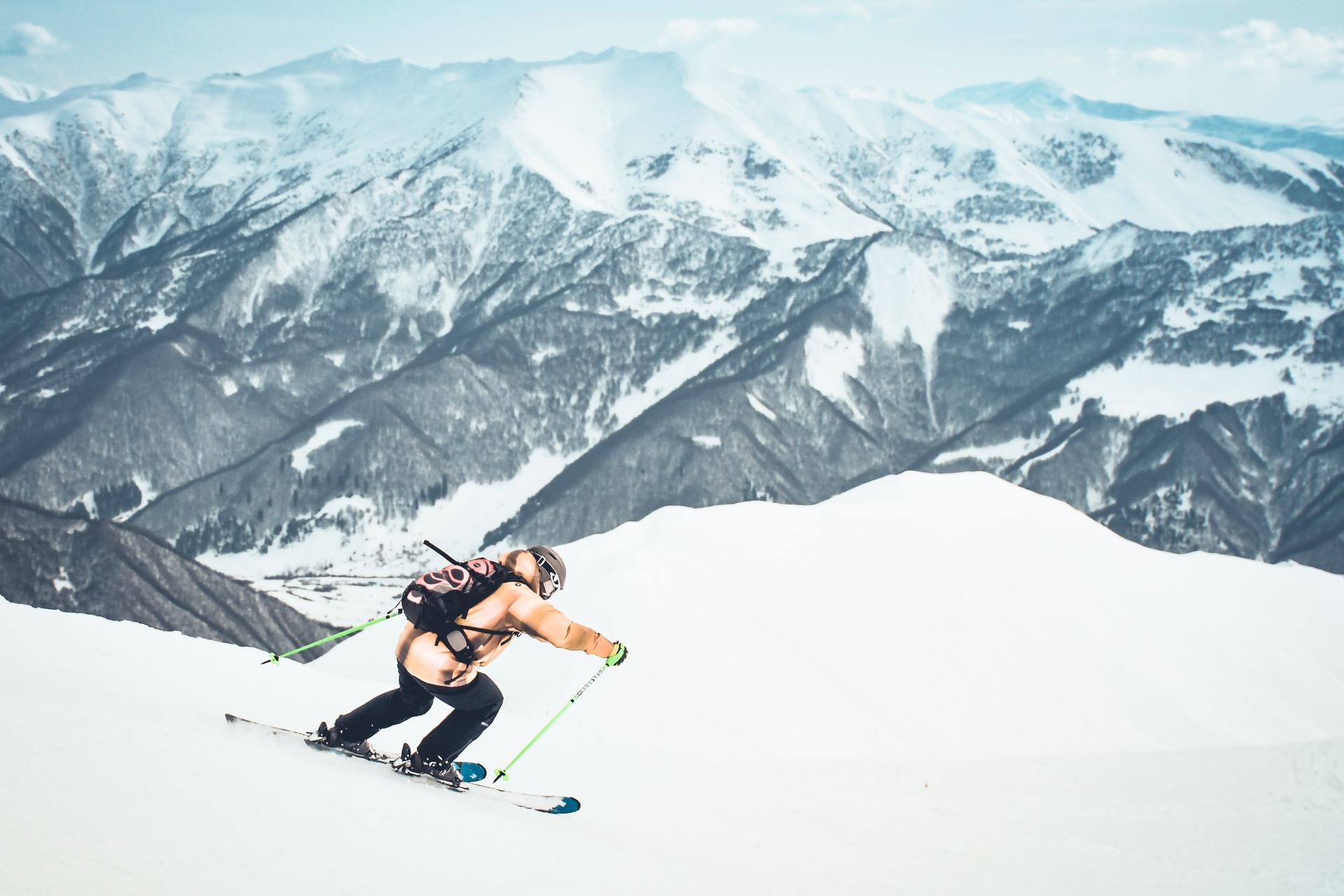 Skier descends a snowy mountain slope with mountains in the background.