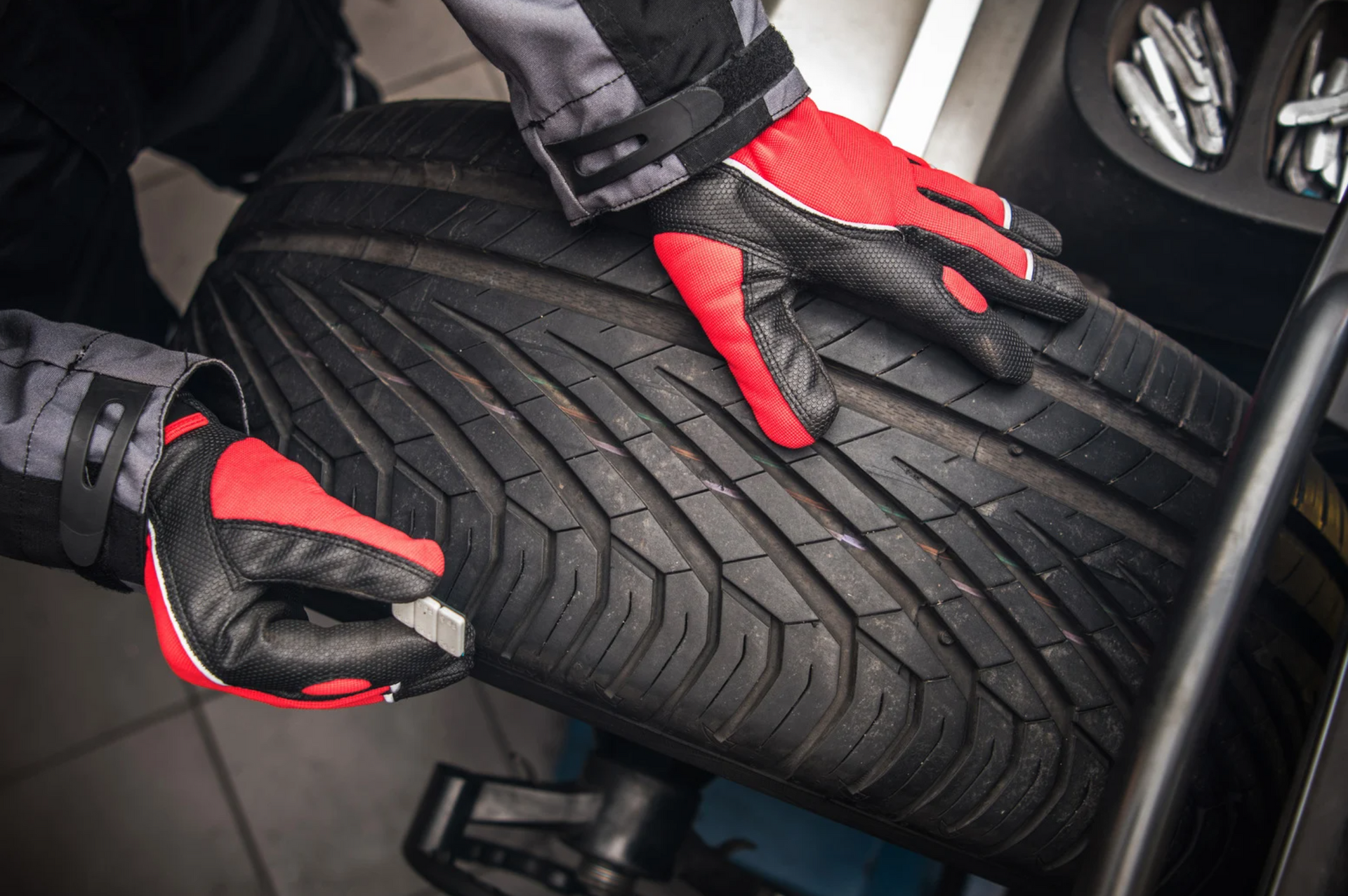 A person wearing red and black gloves is balancing a tire on a machine.