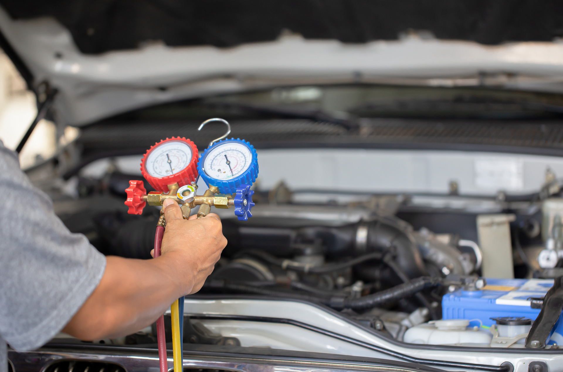 A man is holding two gauges in front of a car engine.