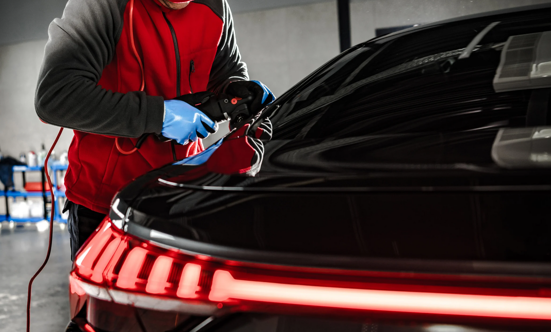 A man is polishing the hood of a black car in a garage.
