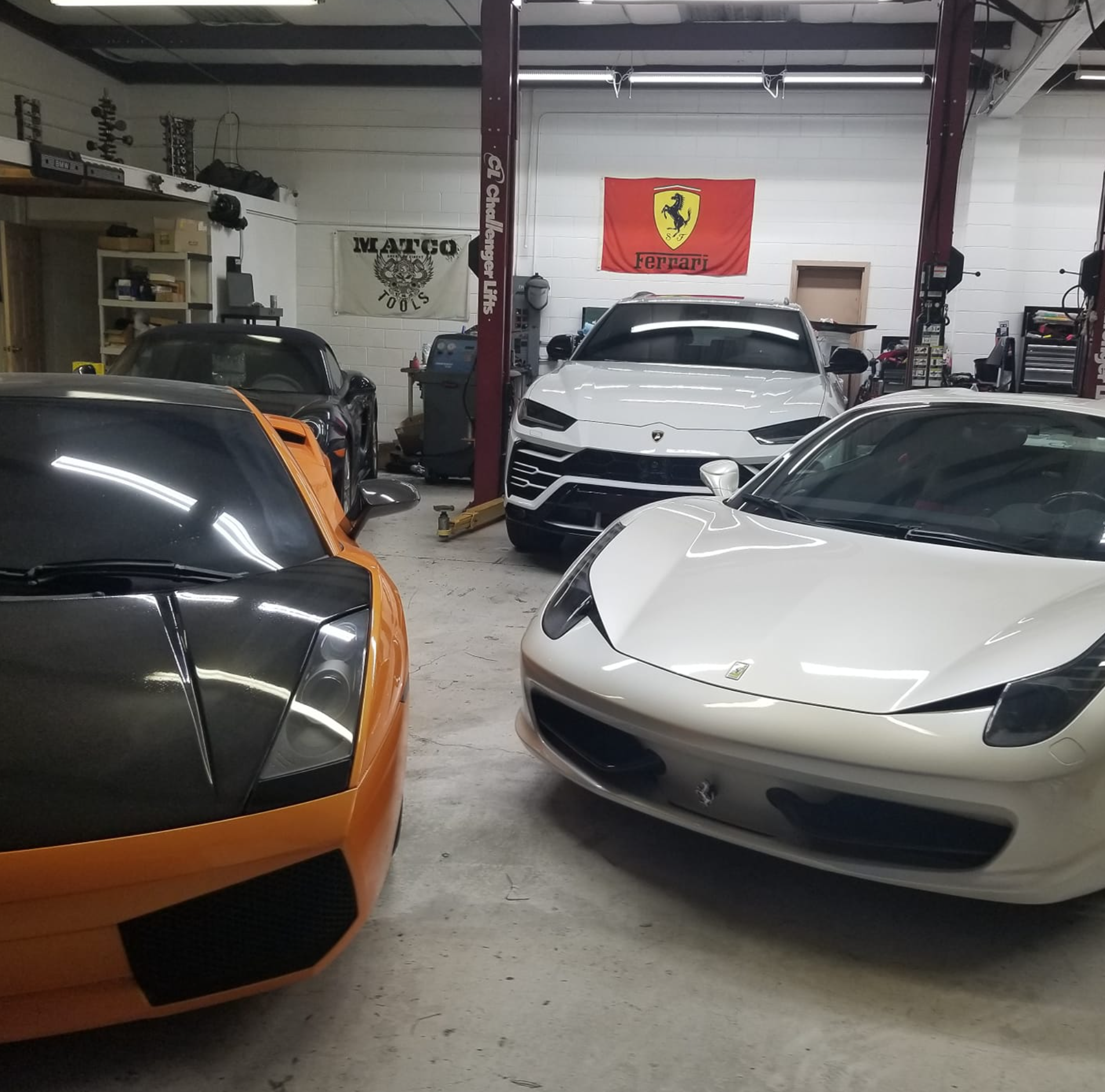 Several cars are parked in a garage with a ferrari flag on the wall