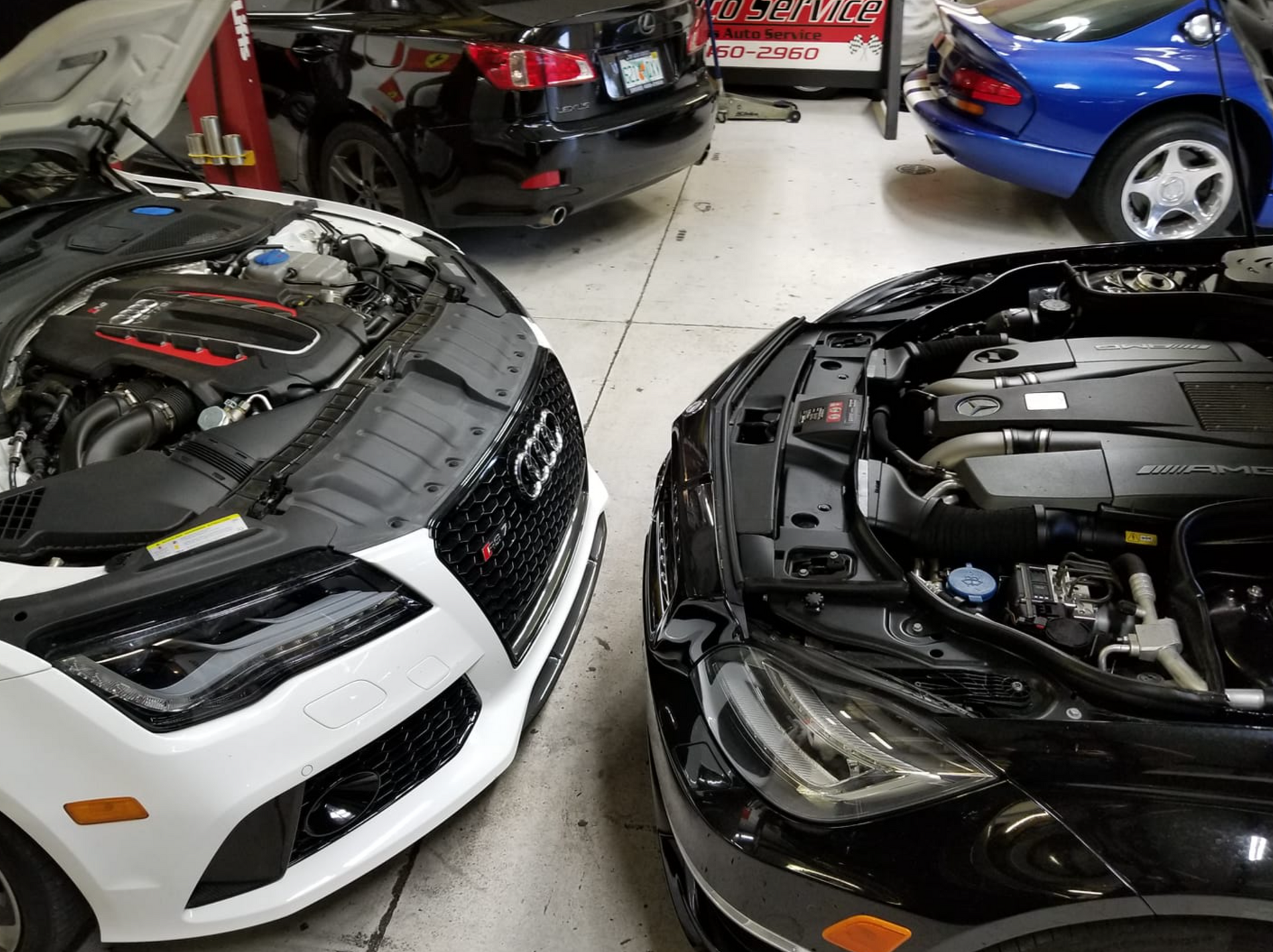 Two cars are parked in a garage with their hoods open