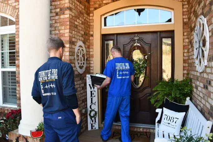 Two men in blue shirts are standing in front of a house holding a welcome sign.