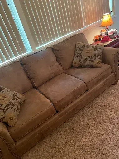 A tan couch is sitting in a living room next to a window.