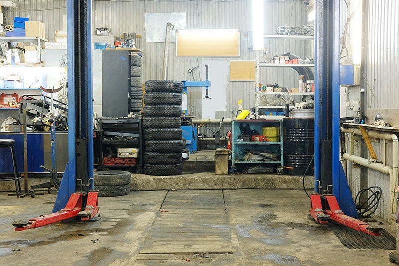 Un pont élévateur dans un atelier de réparation automobile encombré de pneus et d'outils empilés.