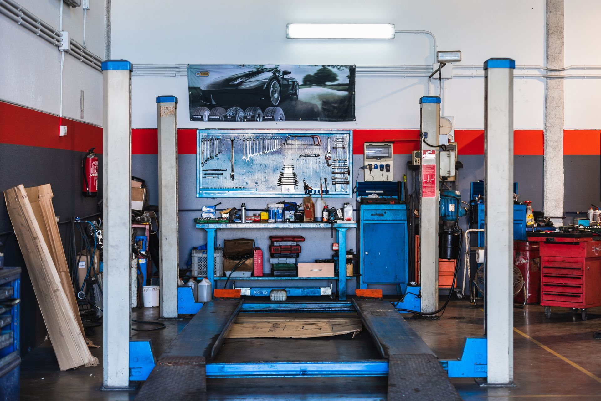 Pont élévateur dans un garage avec outils et établi ; touches de rouge et de bleu.